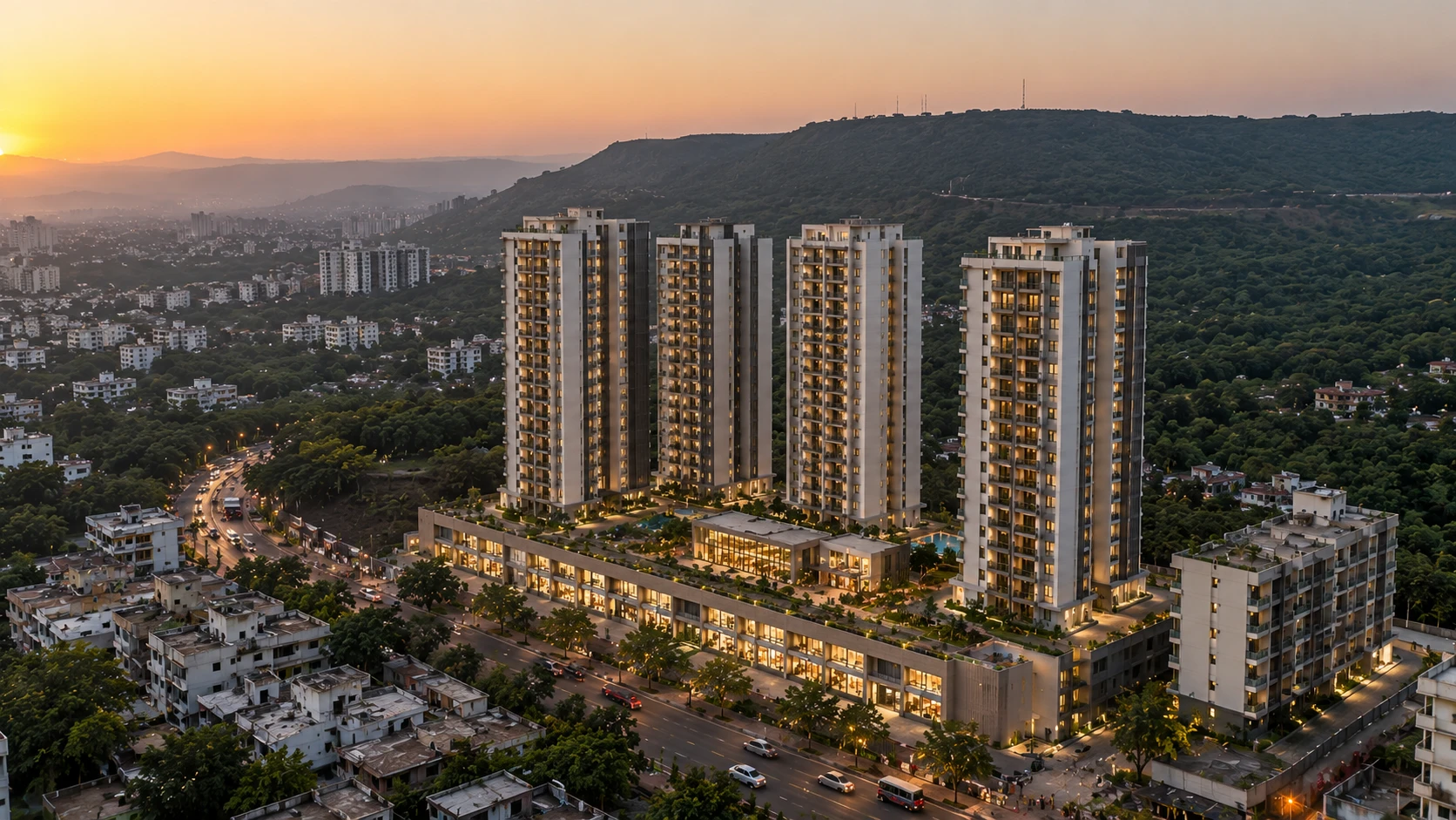 Illustrative aerial render at sunset of four residential towers on a hillside site, a podium of lit showrooms along the main road with gardens and pools on its deck, a smaller housing block beside them, and wooded hills behind